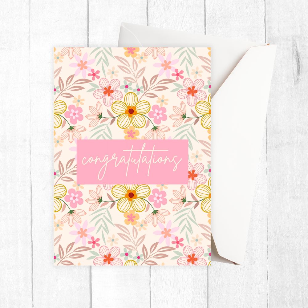 Floral congratulation card with a pink 'congratulations' text on a white wooden surface. Pink Wild Flowers Congratulations Card