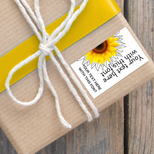 Gift wrapped in brown paper with a yellow ribbon and sunflower-themed label on a wooden surface.SUNFLOWER PERSONALISED GIFT TAG