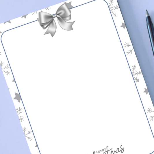 White paper with silver bow and snowflake designs on a blue background. Silver Christmas Notepad A6 stationery