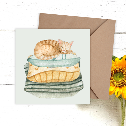Greeting Card with a cat illustration on a stack of books, brown envelope, and sunflower on a wooden surface.