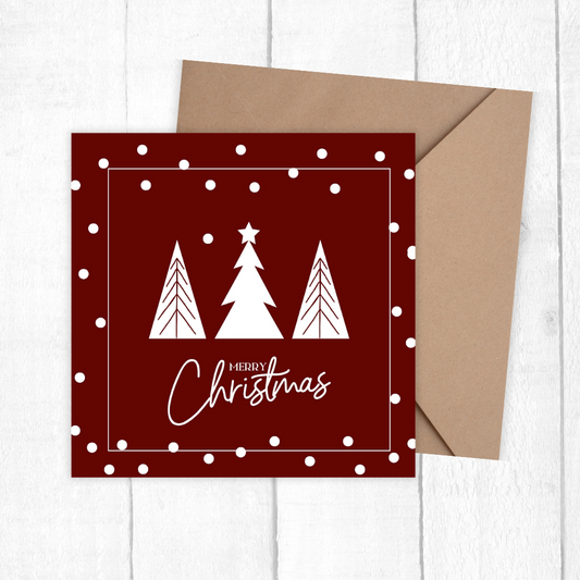 Red Christmas card with white trees and 'Merry Christmas' text, accompanied by a brown envelope on a white wooden surface.Trees Burgundy Christmas Card