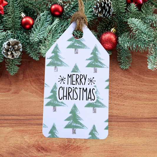 Christmas-themed gift tag with trees and 'Merry Christmas' text, surrounded by festive decorations on a wooden surface.Trees Christmas Gift Tag Set