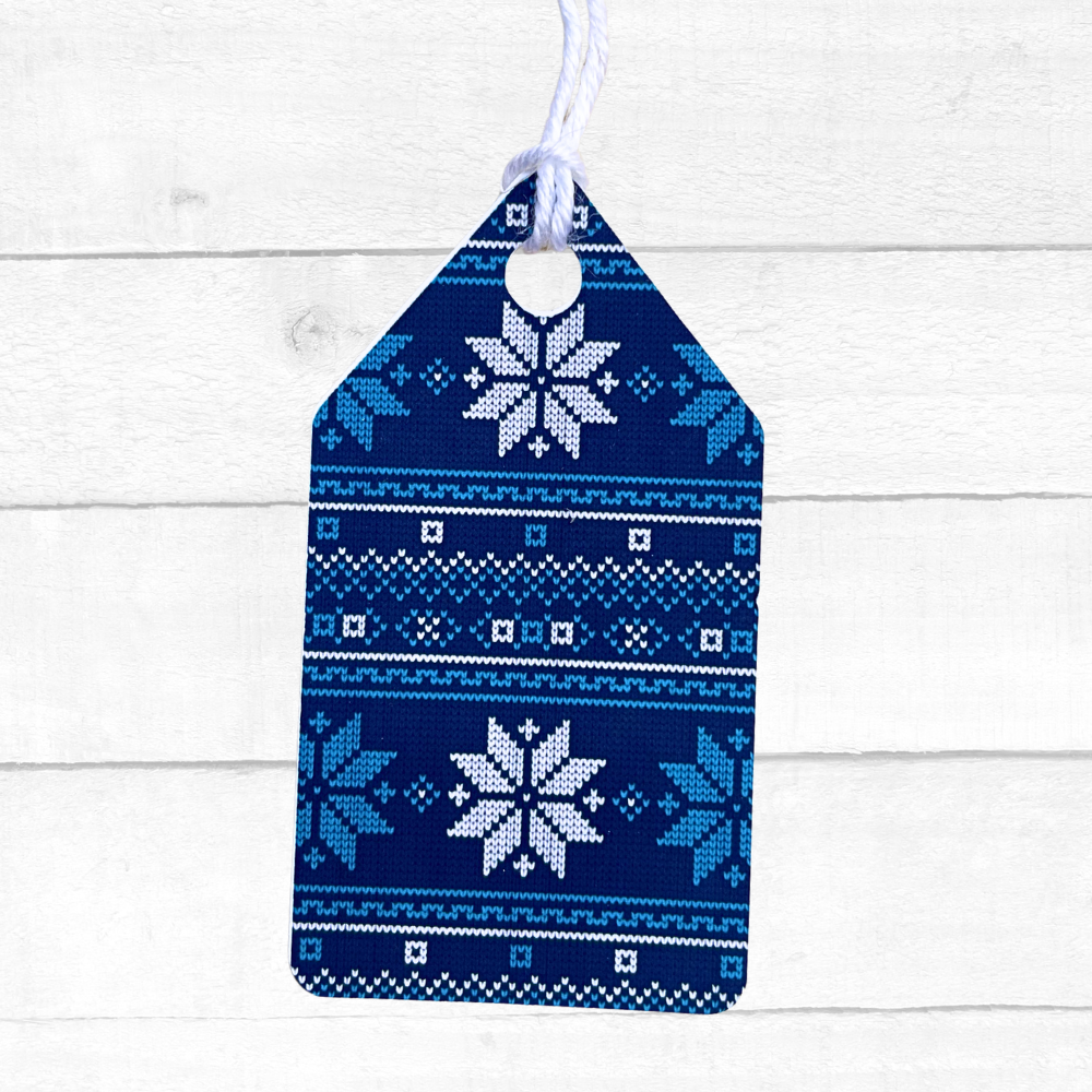 Blue knitted gift tag with white snowflake patterns on a white wooden background. Ugly Sweater Christmas Gift Tag Set