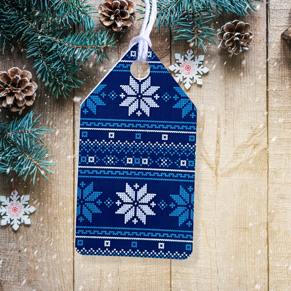 Blue and white patterned Christmas tag with snowflakes on a wooden background with pine branches and cones.Ugly Sweater Christmas Gift Tag Set