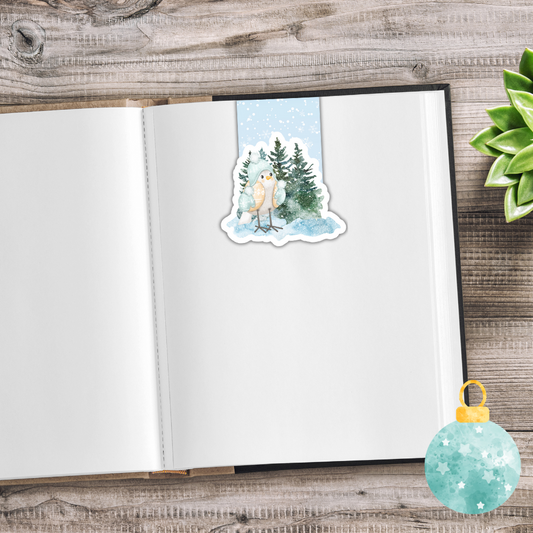 Sticker of a snowy owl and trees on a notebook with a decorative ornament on a wooden surface.White Christmas Magnetic Bookmark Set