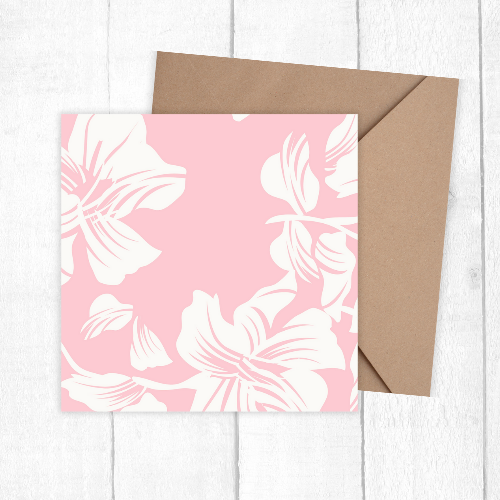 Card with white floral pattern on pink background and brown envelope on white wooden surface. White Flower Happy Birthday Card