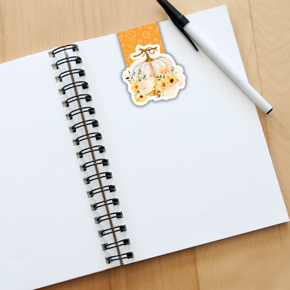 Notebook with a decorative sticker of a pumpkin and flowers on a wooden surface.White Pumpkin Magnetic Bookmark