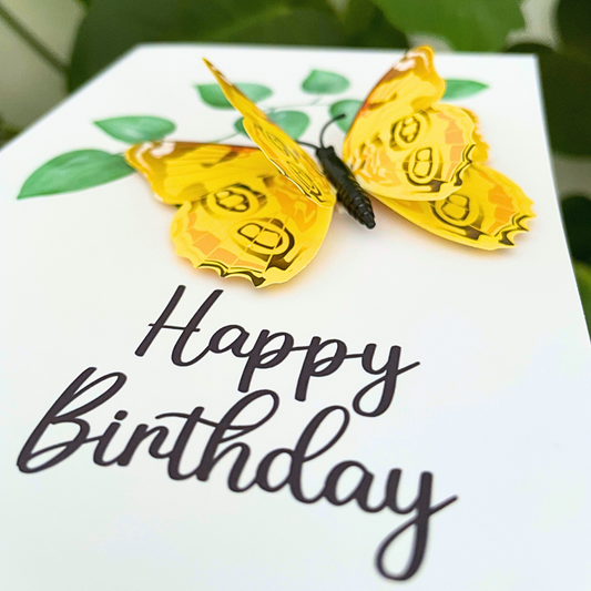 Yellow butterfly earrings on a 'Happy Birthday' card with green leaves.