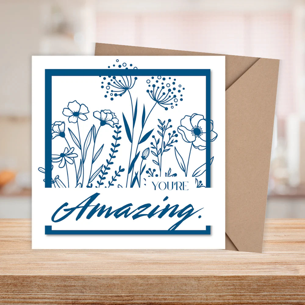 Greeting card with floral design and 'You're Amazing' text on a wooden surface.