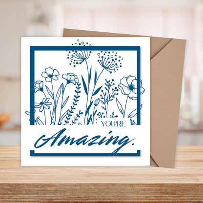 Greeting card with floral design and 'You're Amazing' text on a wooden surface.