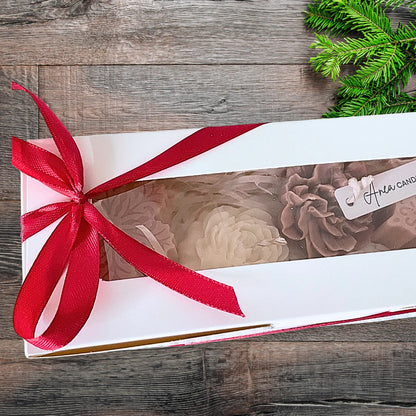 Gift box with a red ribbon on a wooden surface with greenery. CHRISTMAS SPICE CANDLE GIFT BOX