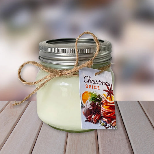 Jar candle labeled 'Christmas Spice' on a wooden surface with a blurred background. CHRISTMAS SPICE NATURAL SOY CANDLE