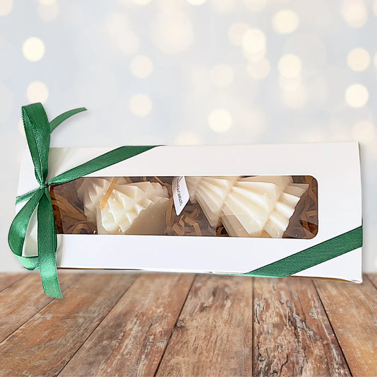 Gift box with white candles and a green ribbon on a wooden surface with a blurred light background. CHRISTMAS TREES CANDLE GIFT BOX