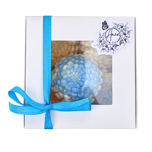 Gift box with a blue ribbon and a decorative item inside, featuring a brand label.chrysanthemum-shaped wax melts