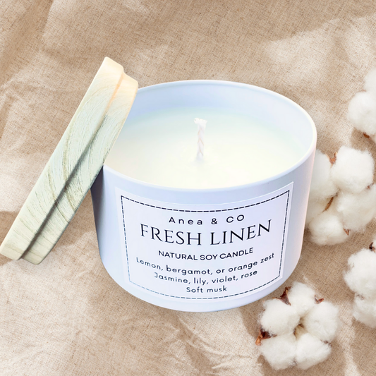 Candle labeled 'Fresh Linen' by Anea & Co on a beige fabric background with cotton fibers. fresh linen natural soy candle