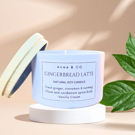 Anea & Co Gingerbread Latte candle on a beige background with green leaves. GINGERBREAD LATTE SOY CANDLE