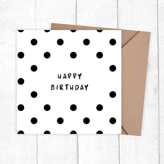 White card with black polka dots and 'Happy Birthday' text, brown envelope on white wooden surface. PASTEL DOTTED BIRTHDAY CARD 