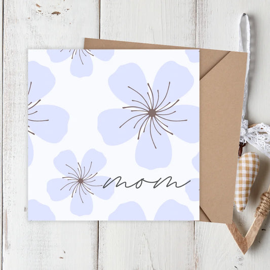 Greeting card with purple flowers and 'mom' text on a wooden surface. PURPLE FLOWERS MOTHER'S DAY CARD