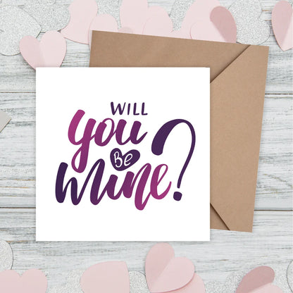 Card with 'Will you be mine?' text on a wooden surface with pink heart decorations. valentine's cards
